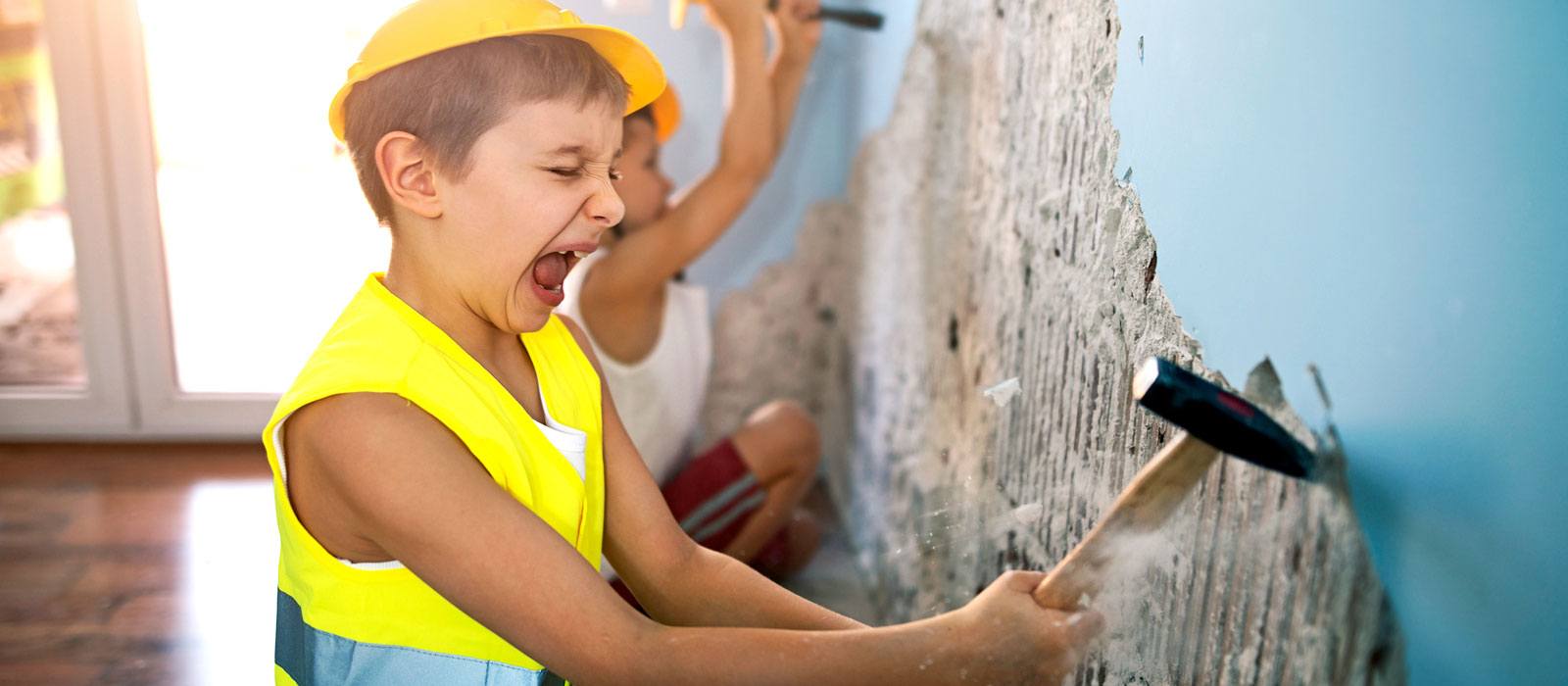 A boy dressed as a construction worker and busting through an old wall.