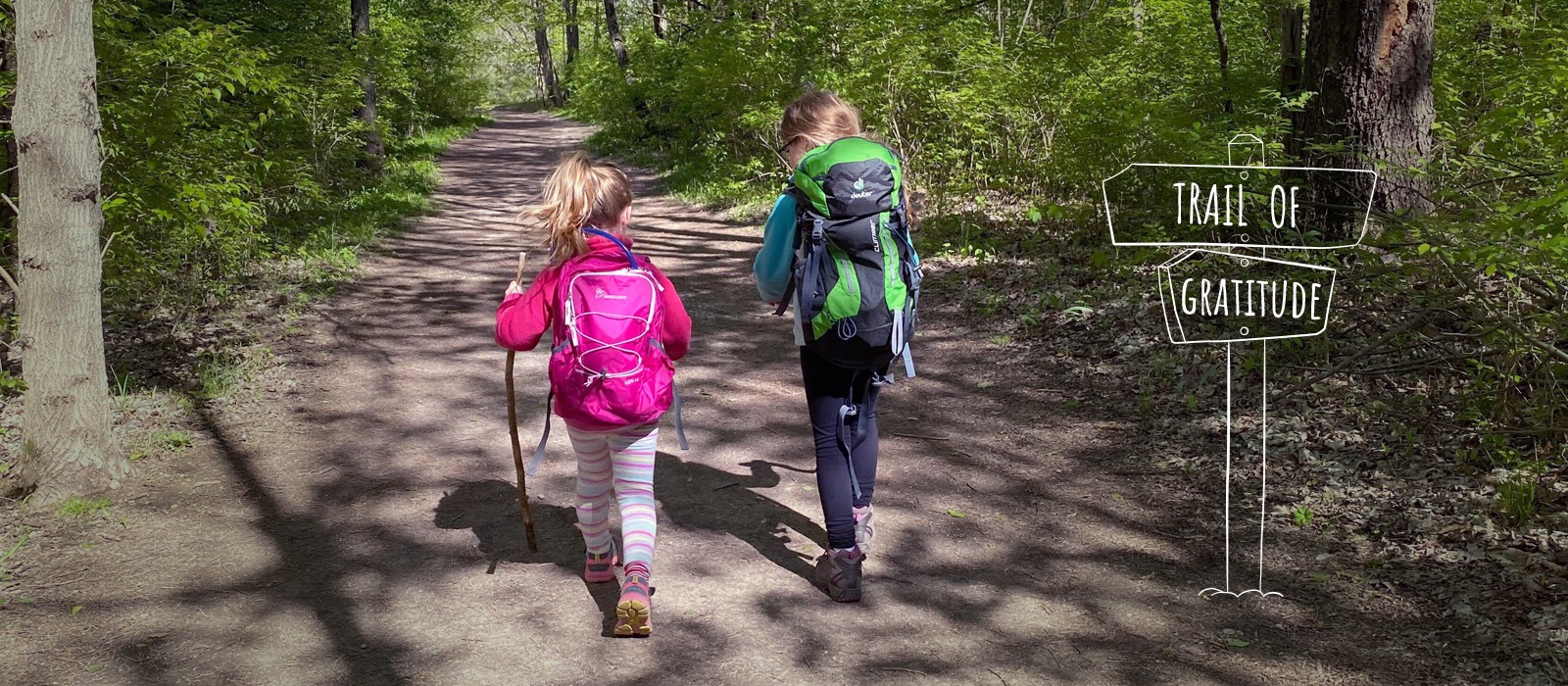 Two little girls with their backpacks and hiking sticks walking on a trail.